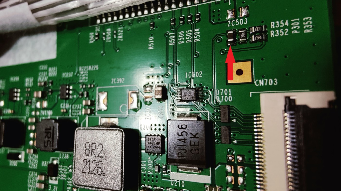 Close-up of the top-right corner of the T-con. A red arrow points at a small upright part with a dark body and no printed code, directly above a gold square pad labeled CN703. Labels R354, R352, P301 and R353 are printed to its right.